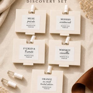 May include: A Maison Elie Parfum Discovery Set featuring five iconic scents. Each scent is presented in a small, rectangular box with a sample vial. The set includes fragrances named Muse Privée, Modern Aristocrat, F*CKED & Fumée, Whiskey Vanilla, and Orange au Miel.