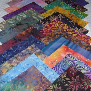 May include: A collection of colorful batik fabric squares arranged in a chevron pattern. The fabrics display a variety of patterns and hues, including blues, greens, purples, and oranges. The designs include floral, abstract, and leaf motifs.