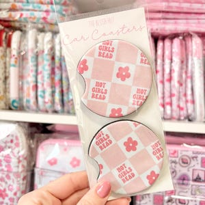 May include: A package of two car coasters with a pink and white checkered pattern. Each coaster has the text "HOT GIRLS READ" and a flower graphic. The packaging reads "THE BLUSH HUT Car Coasters."