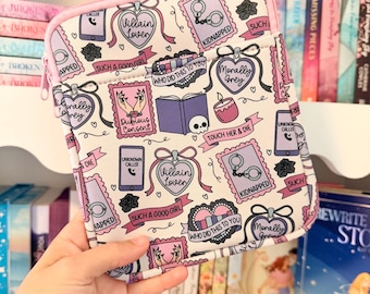 Puede incluir: Una funda rectangular para tableta con fondo blanco que presenta un patrón repetitivo de ilustraciones en morado y rosa, incluyendo esposas, libros, calaveras y teléfonos con textos como Villain Lover, Kidnapped y Morally Grey, con ribete rosa.
