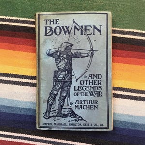 May include: A vintage book cover with a blue background and a black and white illustration of a man in armor shooting an arrow from a bow. The title of the book is "The Bowmen" and the subtitle is "And Other Legends of the War" by Arthur Machen.