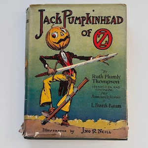 May include: Vintage book cover for "Jack Pumpkinhead of Oz" by Ruth Plumly Thompson, illustrated by J.R. Neill. The cover features a pumpkin-headed character in a red jacket and yellow pants, holding a sword and a rifle. The title is in red and black.