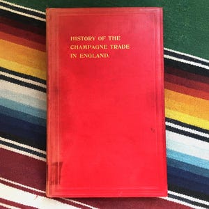 May include: A red hardcover book with the title "HISTORY OF THE CHAMPAGNE TRADE IN ENGLAND."