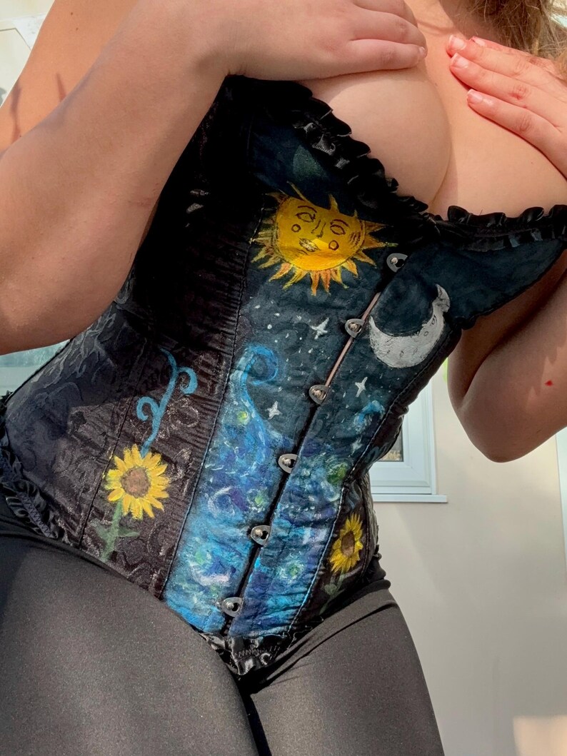 Peut inclure: Un corset noir orn&eacute; d'un motif c&eacute;leste peint &agrave; la main avec un soleil jaune, un croissant de lune blanc et des &eacute;toiles. Le v&ecirc;tement pr&eacute;sente des tourbillons bleus, des tournesols jaunes et un d&eacute;collet&eacute; &agrave; volants avec des fermoirs en m&eacute;tal argent&eacute;.