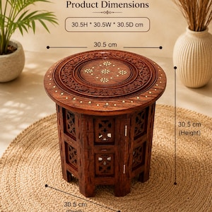 May include: A round wooden side table with intricate floral carvings and inlaid details on the top surface. The table features a lattice-style base and measures 30.5H x 30.5W x 30.5D cm. The wood has a rich brown finish with light-coloured decorative accents.