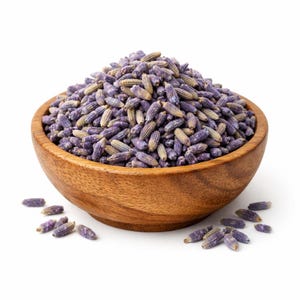 Può includere: Una ciotola di legno piena di boccioli di lavanda essiccati. La lavanda è un mix di viola e marrone chiaro, e alcuni boccioli sono sparsi intorno alla ciotola. La ciotola è di legno marrone chiaro e poggia su una superficie bianca.