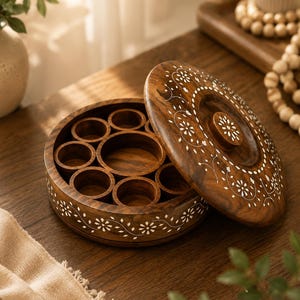 May include: A round, wooden spice box with a lid, featuring a dark brown finish and white floral inlay. The box is open, revealing multiple circular compartments. The lid is partially open, displaying the same floral design.