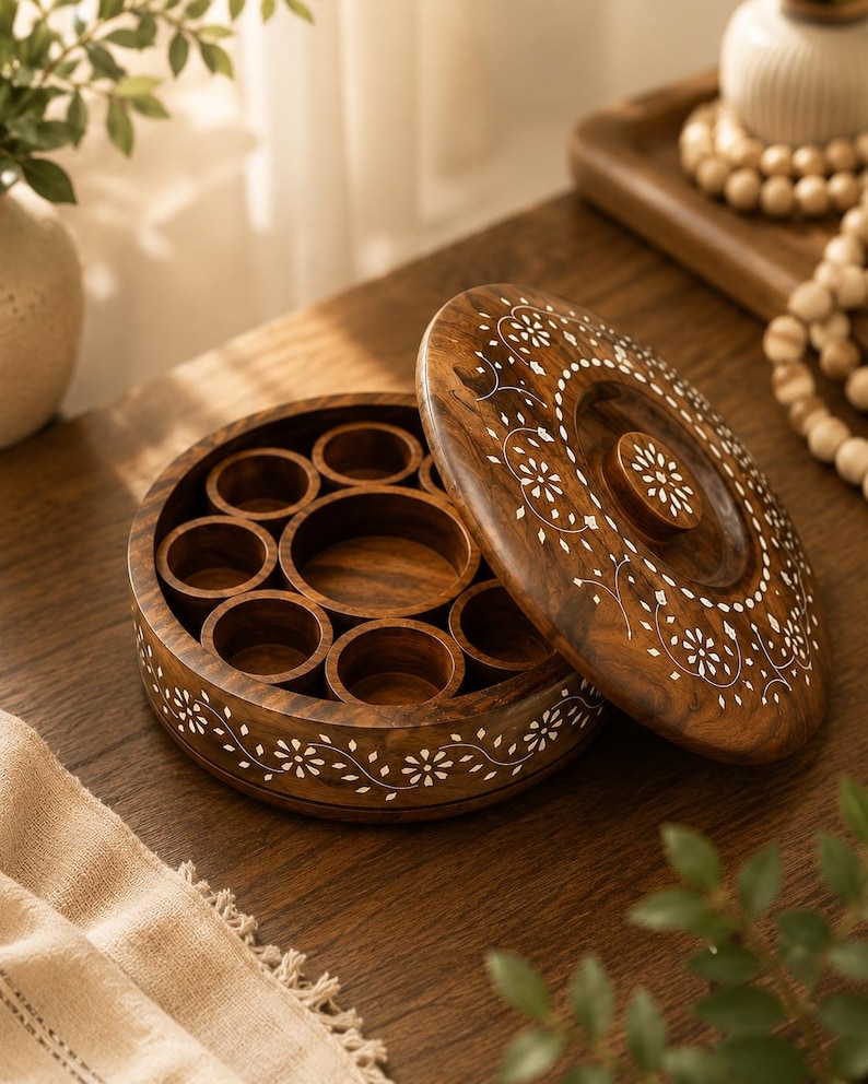 May include: A round, wooden spice box with a lid, featuring a dark brown finish and white floral inlay. The box is open, revealing multiple circular compartments. The lid is partially open, displaying the same floral design.