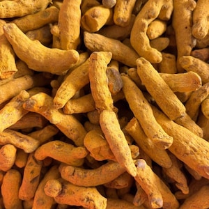 May include: A close-up shot of a pile of dried turmeric roots. The roots are a bright yellow-orange hue, with a textured, uneven surface. The image is tightly framed, filling the view with the spice.