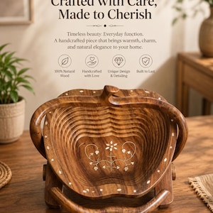 Op de afbeelding: Een handgemaakte houten fruitmand met een uniek ontwerp. De mand is gemaakt van natuurlijk hout en heeft een bloemeninleg. De handvatten zijn gebogen en de mand is opvouwbaar. De tekst "Crafted with Care, Made to Cherish" staat bovenaan.