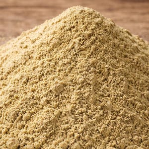 Könnte beinhalten: Nahaufnahme eines Haufens hellbraunen Pulvers, möglicherweise ein Gewürz oder eine Zutat zum Kochen. Das feine, körnige Pulver liegt auf einer Holzoberfläche.