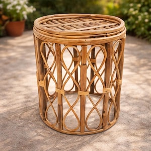 May include: A round, natural-toned rattan side table. The table features a woven top and a decorative openwork design on the sides. The table is approximately 18 inches in height and 16 inches in diameter, suitable for outdoor or indoor use.