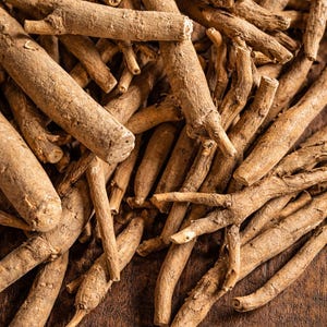 May include: Close-up of ashwagandha roots, showcasing their natural, light brown color and textured surface. The roots are arranged on a dark wooden surface, highlighting their organic form. A visual representation of a natural herb.