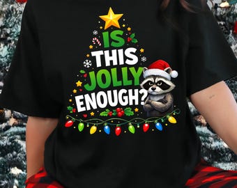 May include: Black crew neck t-shirt with a Christmas tree design and the text "IS THIS JOLLY ENOUGH?". The design includes a raccoon wearing a Santa hat. The person is wearing red and black plaid pajama pants.