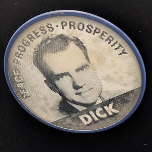 Może przedstawiać: Okrągła odznaka kampanii z niebieską obwódką. Odznaka przedstawia czarno-biały portret mężczyzny i imię "DICK" pogrubionymi białymi literami. Słowa "PEACE - PROGRESS - PROSPERITY" są wydrukowane wokół portretu.