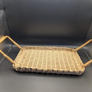 May include: A rectangular woven wicker tray with two bamboo handles. The tray is light brown and has a woven pattern. The handles are a lighter shade of brown and are attached to the sides of the tray.