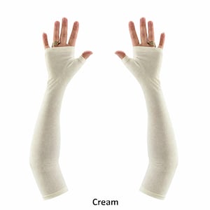 May include: A pair of cream-coloured fingerless arm sleeves that extend from the knuckles to the upper forearm. These sleeves feature a thumb hole opening and a smooth, solid fabric construction, providing full arm coverage in a neutral tone.