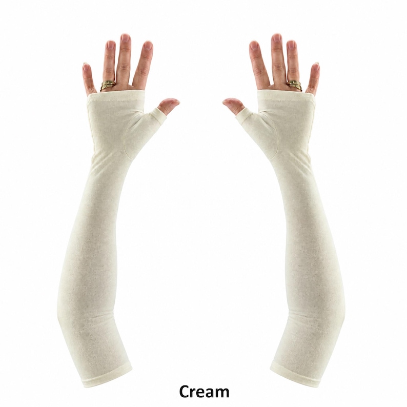 May include: A pair of cream-coloured fingerless arm sleeves that extend from the knuckles to the upper forearm. These sleeves feature a thumb hole opening and a smooth, solid fabric construction, providing full arm coverage in a neutral tone.