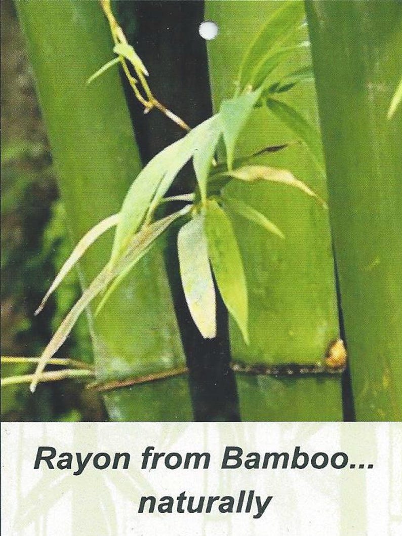 Puede incluir: Una vista de cerca de tallos de bamb&uacute; verdes y hojas delgadas con un tallo central oscuro. Debajo de la imagen de la planta, una etiqueta rectangular blanca presenta el texto impreso en negro: Rayon from Bamboo... naturally. Incluye un peque&ntilde;o orificio.