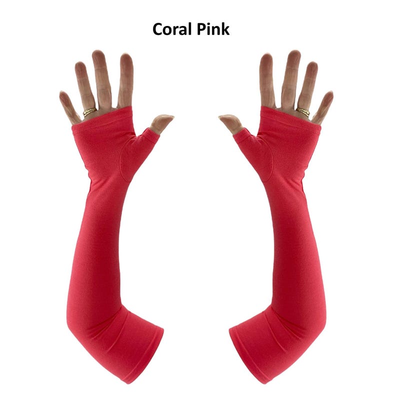 May include: A pair of coral pink fingerless arm sleeves that extend from the knuckles to the forearm. The fabric is a solid, smooth material with a thumb hole opening. The text Coral Pink is displayed at the top centre of the image.