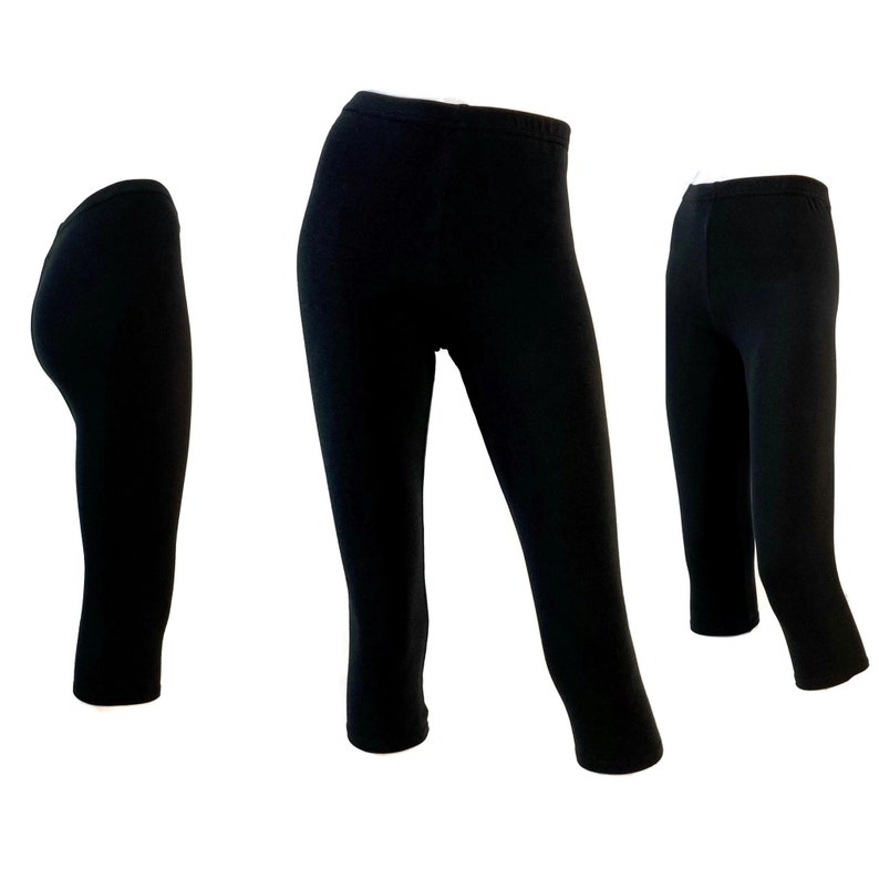 Puede incluir: Tres pares de leggings negros lisos mostrados desde diferentes &aacute;ngulos. Cada par presenta una cintura alta y una silueta ajustada que termina debajo de la rodilla. Los leggings se muestran sobre un fondo blanco liso.