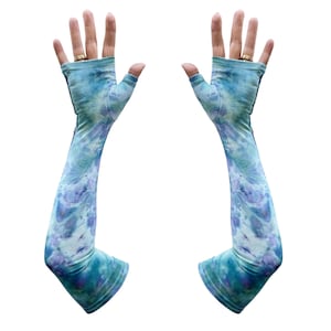 Puede incluir: Un par de mangas largas sin dedos con un estampado tie-dye en tonos azules, turquesas y morados. Las mangas cubren los brazos desde la muñeca hasta la parte superior del brazo, con un agujero para el pulgar.