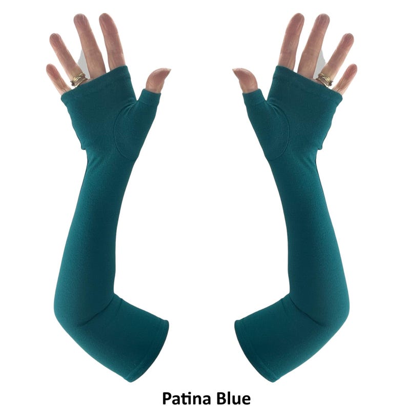 May include: A pair of fingerless gloves in a solid patina blue colour. These long, arm-covering gloves feature an opening for the thumb and extend past the wrist, providing coverage up to the forearm with a smooth, seamless fabric construction.