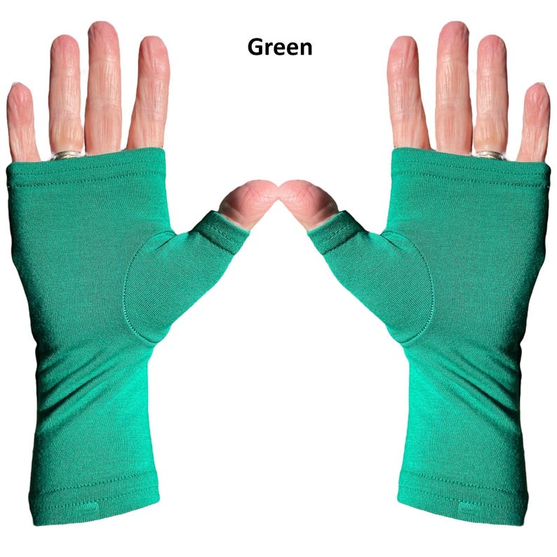 May include: A pair of fingerless gloves in a solid green color. The gloves feature a thumb hole and extend from the knuckles down to the wrist, with a simple hemmed edge at both the top and bottom openings. The word Green is printed above.