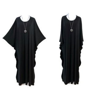Peut inclure: Deux images d'une robe caftan noire avec de larges manches et un ourlet jusqu'au sol. La robe a une encolure ronde et est accessoirisée d'un collier pendentif argenté. Le tissu est ample, créant une silhouette fluide. Le fond est blanc uni.