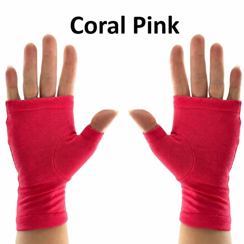 May include: A pair of fingerless gloves in a solid coral pink color. The gloves feature a thumb hole and cover the palm and wrist area, leaving the fingers exposed. The text "Coral Pink" is printed in black above the gloves.