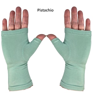 May include: A pair of fingerless gloves in a solid pistachio green color. The gloves feature a thumb hole and cover the palm and wrist area, with a stitched hem at the top and bottom edges. The text "Pistachio" is printed above the gloves.