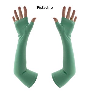 May include: A pair of pistachio green fingerless arm sleeves that extend from the knuckles to the forearm. The sleeves feature a thumb hole and a smooth, solid-coloured fabric construction. The text "Pistachio" is printed above the sleeves.