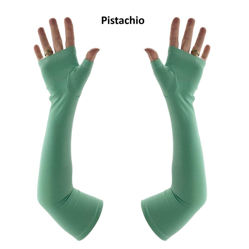 May include: A pair of pistachio green fingerless arm sleeves that extend from the knuckles to the forearm. The sleeves feature a thumb hole and a smooth, solid-coloured fabric construction. The text "Pistachio" is printed above the sleeves.