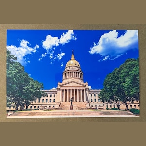 Peut inclure: Photographie du Capitole de l'État de Virginie-Occidentale. Le bâtiment beige est surmonté d'un dôme doré, sur fond de ciel bleu vif avec des nuages blancs et duveteux. Des arbres verts luxuriants encadrent les côtés du bâtiment.