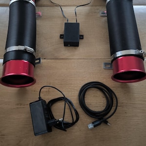 May include: Two black cylindrical tubes with red flared ends, secured by metal hose clamps. A small black rectangular control box with wires, a black power adapter with a cord, and a separate black USB cable are included in this set.