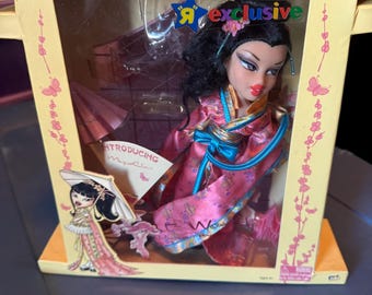 May include: Bratz World! Collector's Edition doll in a box. The doll is wearing a pink kimono with blue accents. The box is yellow with pink floral and butterfly designs. The text "R exclusive" is visible on the box.