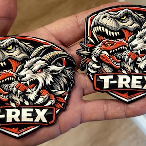 May include: Two shield-shaped patches featuring a T-Rex dinosaur, a snarling wolf, and a red dragon. The patches have a black, white, and red color scheme with the text "T-REX" in a white, bold font.