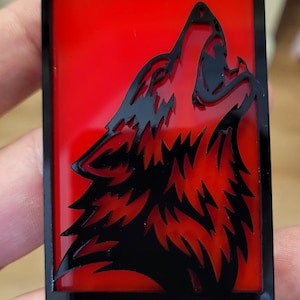 May include: A rectangular black and red emblem featuring a howling wolf silhouette. The wolf is black, set against a red background. The word "COYOTE" is displayed in red block letters at the bottom of the emblem.