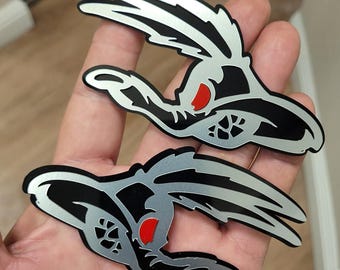 May include: Two stylized, black and silver decals in a rabbit-like design with red accents. The decals have a glossy finish and are likely for automotive or decorative use. The design features sharp lines and a modern aesthetic.