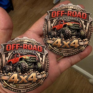 May include: Two circular metallic emblems featuring a red off-road truck with large tyres. The text reads OFF-ROAD PERFORMANCE and 4x4, with MUD DIRT POWER inscribed along the gear-shaped border. The design has a weathered bronze finish.