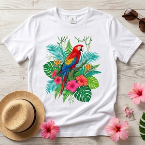 May include: A white short-sleeve t-shirt featuring a vibrant graphic of a red, yellow, and blue macaw parrot perched on a branch, surrounded by green tropical palm leaves, ferns, and bright pink hibiscus flowers centered on the chest.