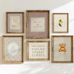 May include: A collection of framed art prints with vintage-style designs. The prints feature a goose with ducklings, a sunflower, a teddy bear, an alphabet, and text that reads "You are my sunshine" and "how lucky are we". The frames are gold-colored.