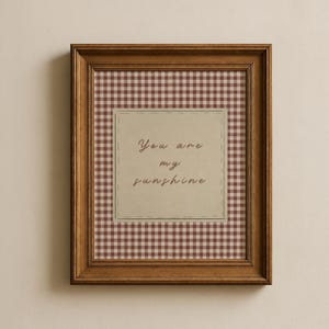 May include: A framed print with a brown wooden frame. The print features a gingham pattern in shades of brown and cream. A central square contains the handwritten text "You are my sunshine."