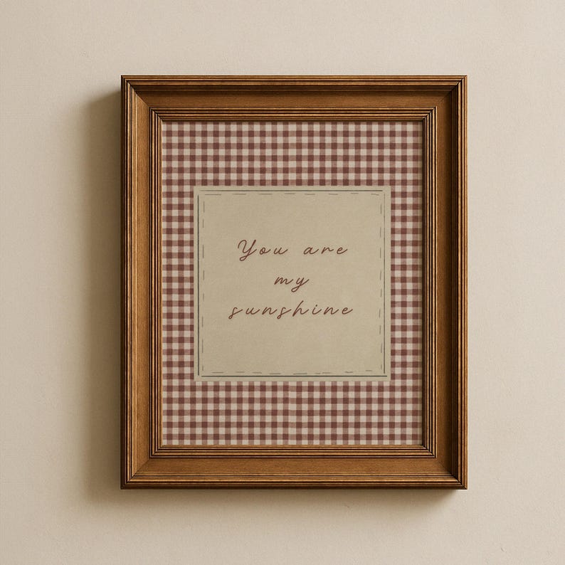 May include: A framed print with a brown wooden frame. The print features a gingham pattern in shades of brown and cream. A central square contains the handwritten text "You are my sunshine."