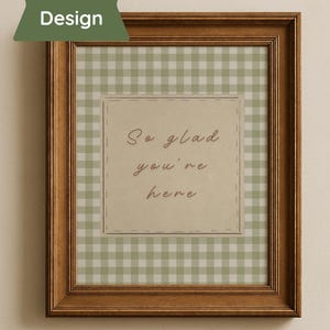 May include: A framed print with a brown wooden frame. The print features a green and white gingham pattern background. A central square has the text "So glad you're here" in a handwritten style font. A green banner in the upper left corner says "Bonus Design".
