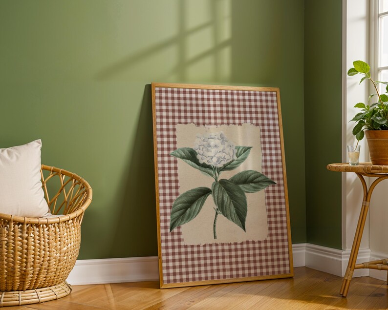 May include: A framed botanical print of a white hydrangea flower with green leaves. The artwork is set against a cream background and framed with a brown and white gingham pattern. The frame is a light wood colour.