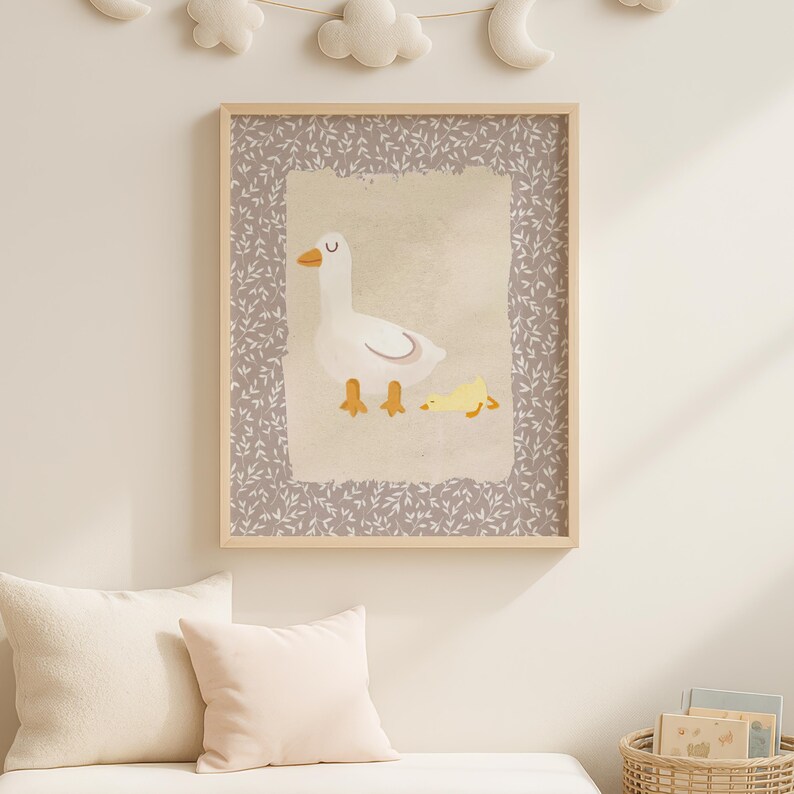 May include: A framed print featuring a white goose with yellow feet and a yellow gosling. The artwork has a light beige background with a gray floral border. The frame is light wood. The print is hanging on a light beige wall.