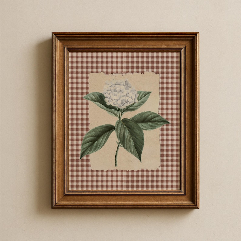 May include: A framed botanical print of a white hydrangea flower with green leaves. The artwork is set against a tan background with a torn edge, over a brown and white checkered pattern. The frame is made of brown wood.