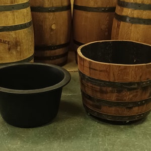 Pu&ograve; includere: Quattro barili di legno con fasce metalliche, di cui due utilizzati come fioriere con rivestimenti in plastica nera. I barili sono su un pavimento verde.