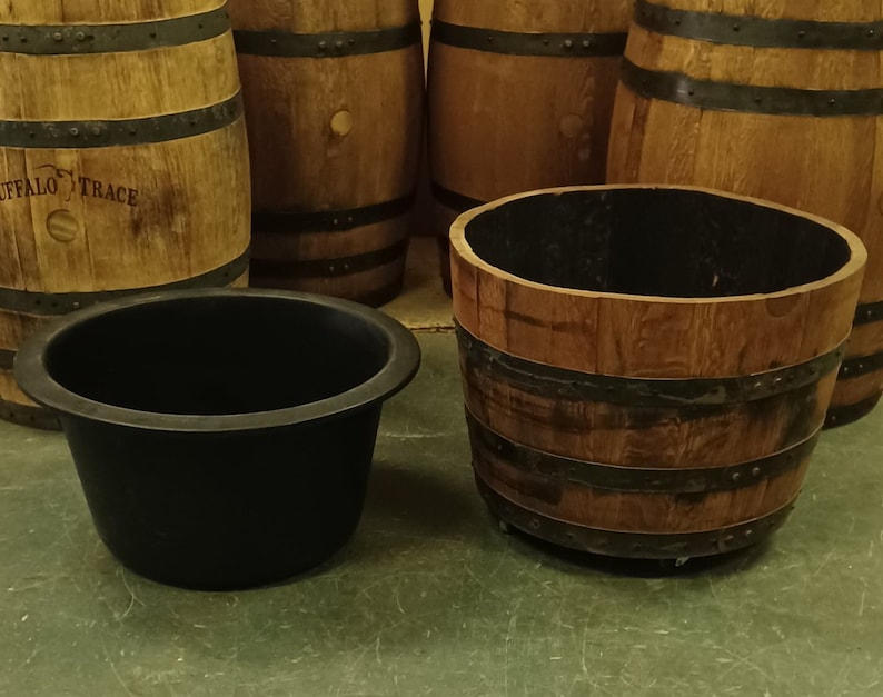 Pu&ograve; includere: Quattro barili di legno con fasce metalliche, di cui due utilizzati come fioriere con rivestimenti in plastica nera. I barili sono su un pavimento verde.